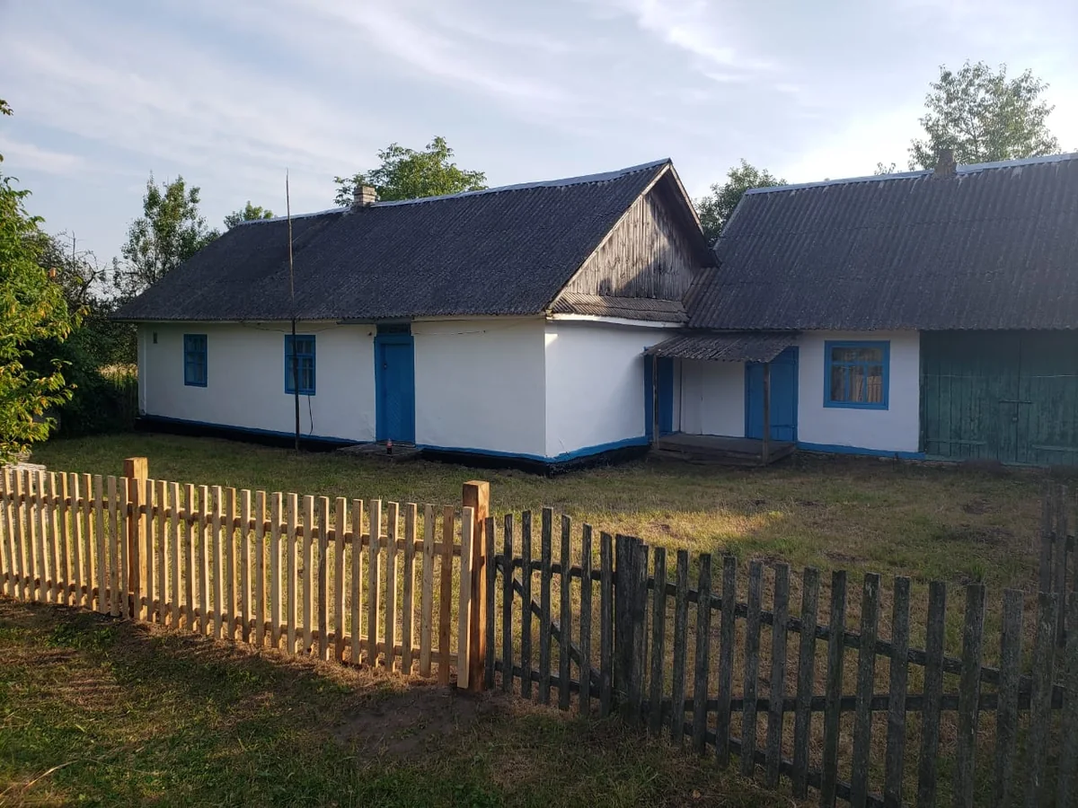 Dom Babci: białe ściany, niebieskie okna i drewniany płot